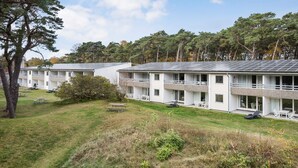 A row of modern, two-story buildings with balconies, surrounded by a grassy area and trees.