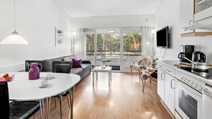 A modern living room with a sofa, a dining table, and a kitchen area with a stove and a TV.