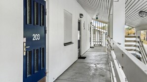 A corridor with a blue door labeled "203", white walls, and a white railing on the right.