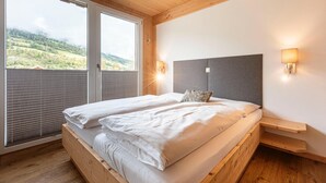 Una cama doble con cabecera gris, dos lámparas de noche y una mesita de noche de madera.