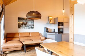 Una sala acogedora con sofá, una mesa de madera y una cocina equipada con electrodomésticos modernos.