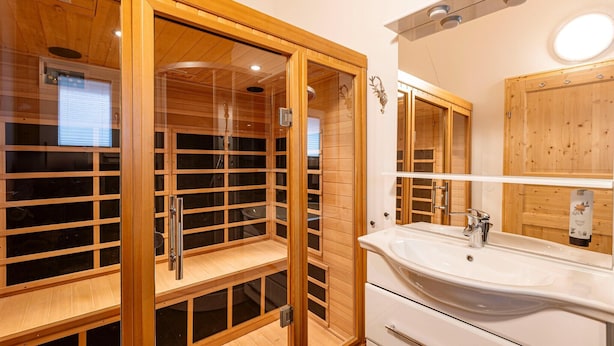 Un baño moderno con sauna de madera, un lavabo grande y un espejo.