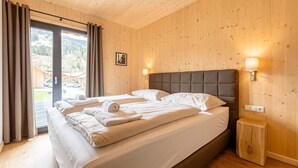 Ein Schlafzimmer mit einem großen Bett, Holzwänden und Blick auf eine Berglandschaft durch eine Schiebetür.