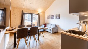 Una cocina moderna con piso de madera, un comedor con mesa y sillas, un sofá gris y un ventanal con cortinas.
