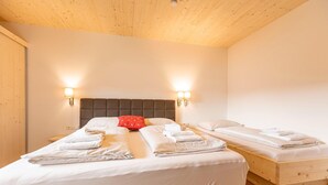 Un dormitorio con una cama grande, dos camas más pequeñas, techo de madera y luces empotradas en la pared.