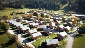A cluster of wooden cabins with pitched roofs, arranged in rows, surrounded by green fields and hills.