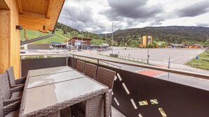 Un balcone con mobili in vimini e un tavolo in vetro con vista su una strada e degli edifici.