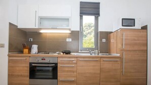 Eine moderne Küche mit Holzschränken, einem eingebauten Backofen, einer Mikrowelle und einem Fenster mit Blick auf Grünflächen.