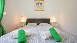 Ein Doppelbett mit gemustertem Bettbezug, zwei Kissen, zwei Nachttische mit Lampen und ein gerahmtes Bild an der Wand.