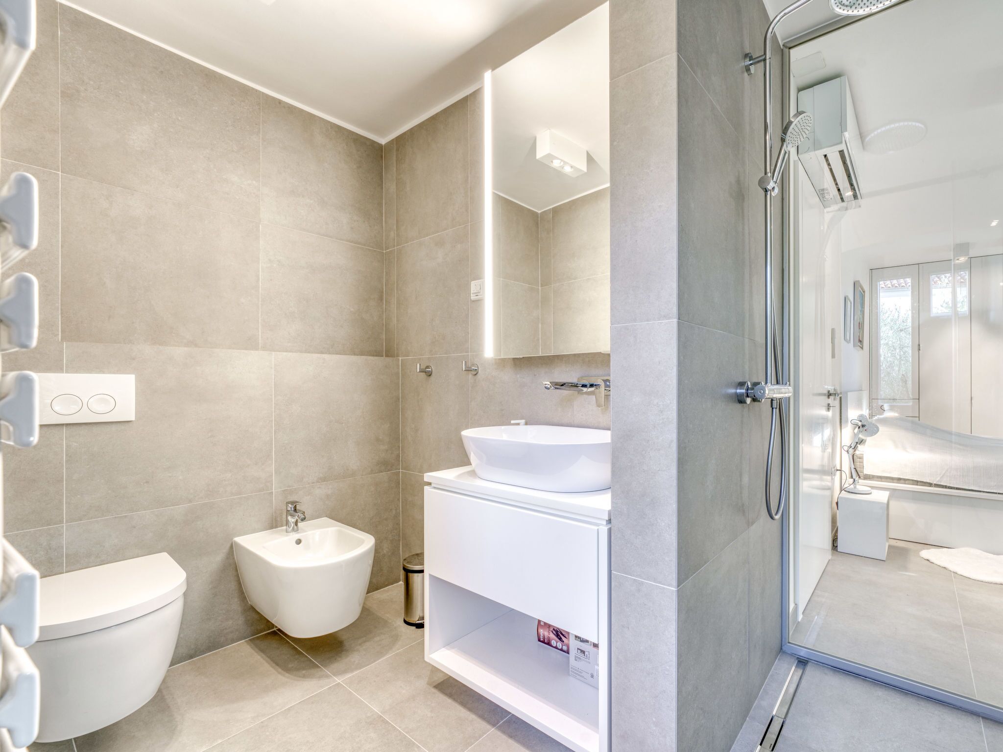 A modern bathroom with a bidet, a sink, and a shower.