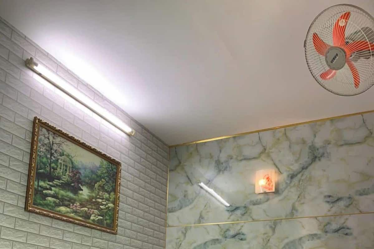 A hotel room with a bed, a painting on the wall, a marble-patterned wall, and a ceiling fan.