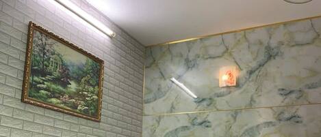 A hotel room with a bed, a painting on the wall, a marble-patterned wall, and a ceiling fan.