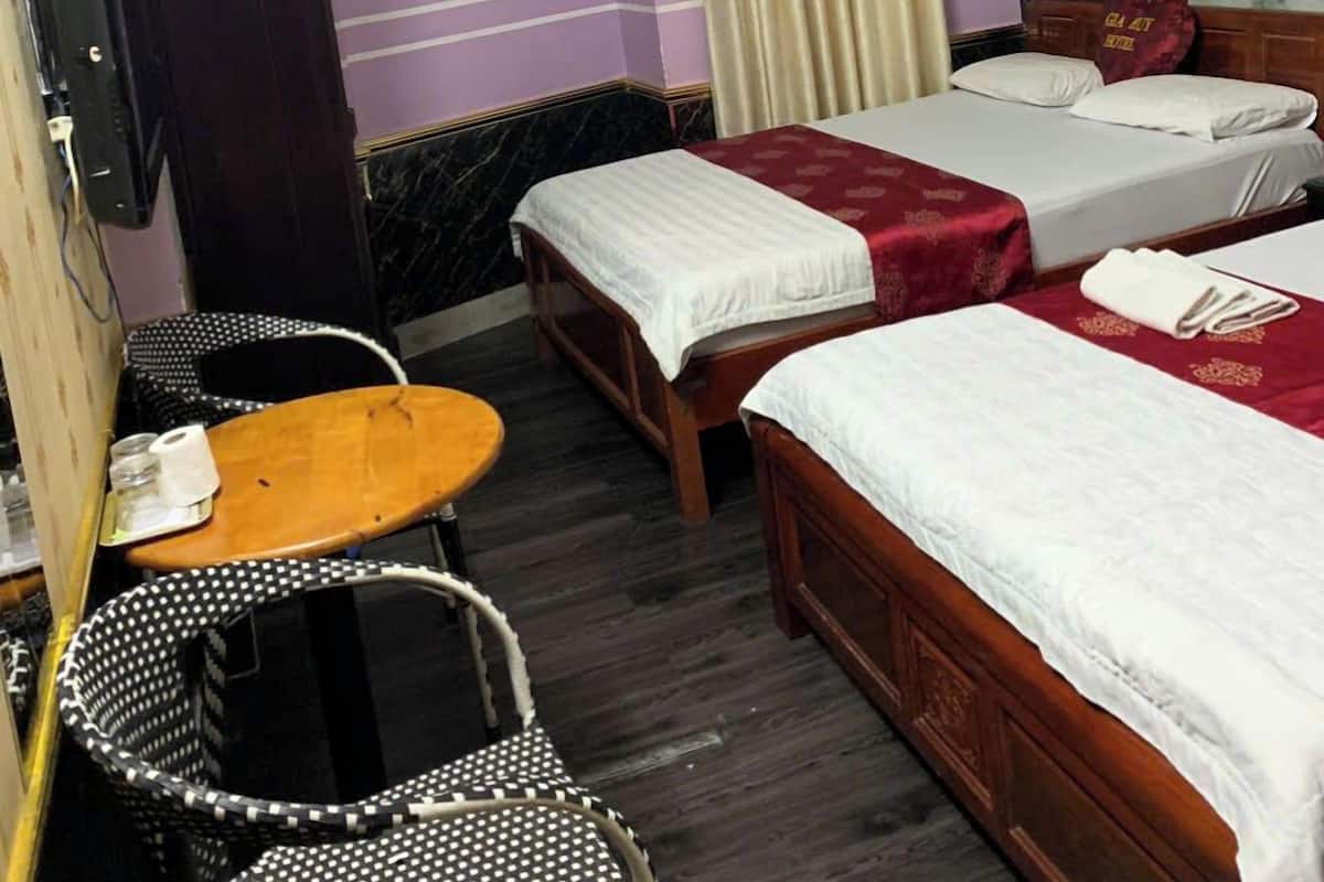 A hotel room with two single beds, a wooden table, a small round table, a TV, a sign on the door, and a painting on the wall.