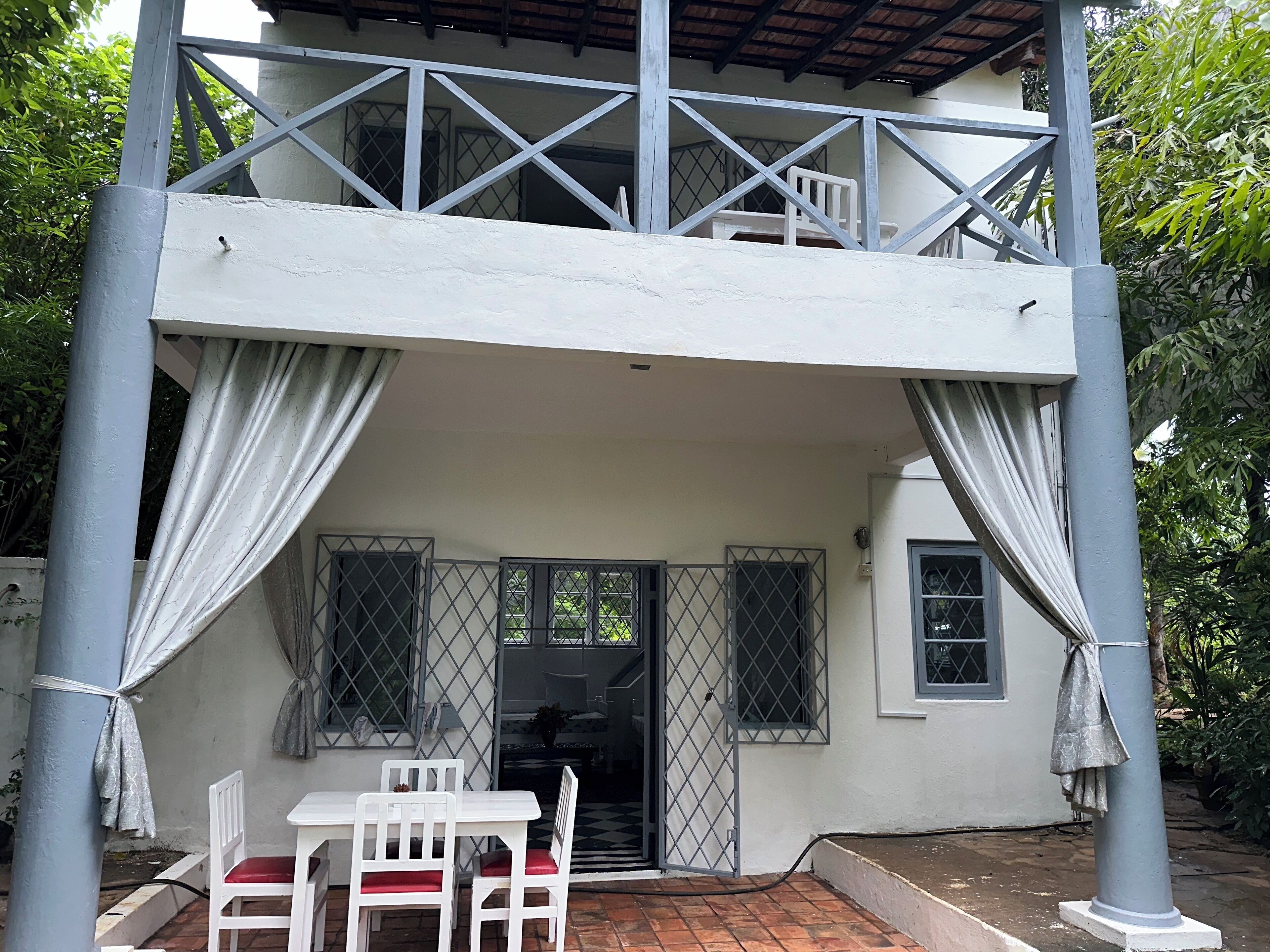 A two-story building with a balcony, white walls, and a tiled patio area with a table and chairs.