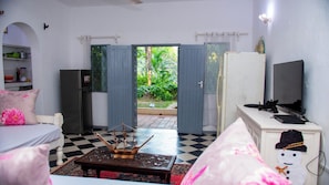 A room with a checkered floor, a wooden table, a bed with pink pillows, a television on a white cabinet, and a door leading outside. - Cosy beach villa (Malindi)