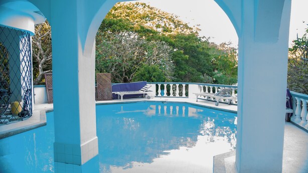 A pool area with a clear blue pool, white balustrades, and a view of trees and foliage in the background. - Cosy beach villa (Malindi)