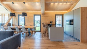 A modern kitchen with a central island, wooden ceiling, and large windows. - Superior Holiday Home with Sauna (Haus im Ennstal)