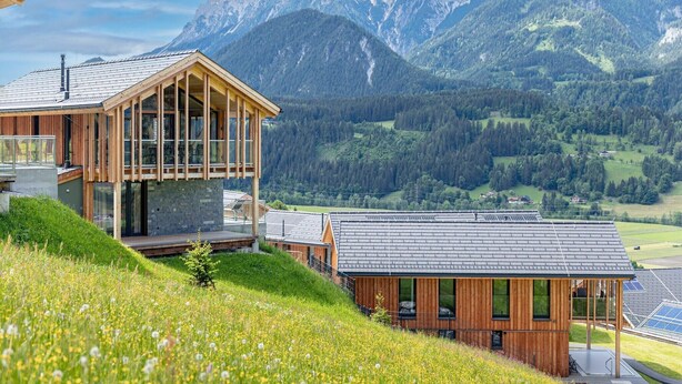 A modern wooden cabin with large windows, a balcony, and solar panels, set against a mountainous backdrop. - Superior Holiday Home with Sauna (Haus im Ennstal)
