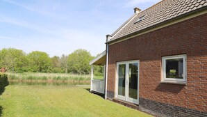 A brick house with a large glass door and windows, a grassy yard, and a pond in the background. - Bungalow in Zuytland Buiten by the Water (Simonshaven)