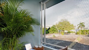 A room with a laptop on a small table, a wicker tray with bowls, a potted plant, and a view through a window with a mesh screen. - Comfy Corner Hotel (Chiang Mai)