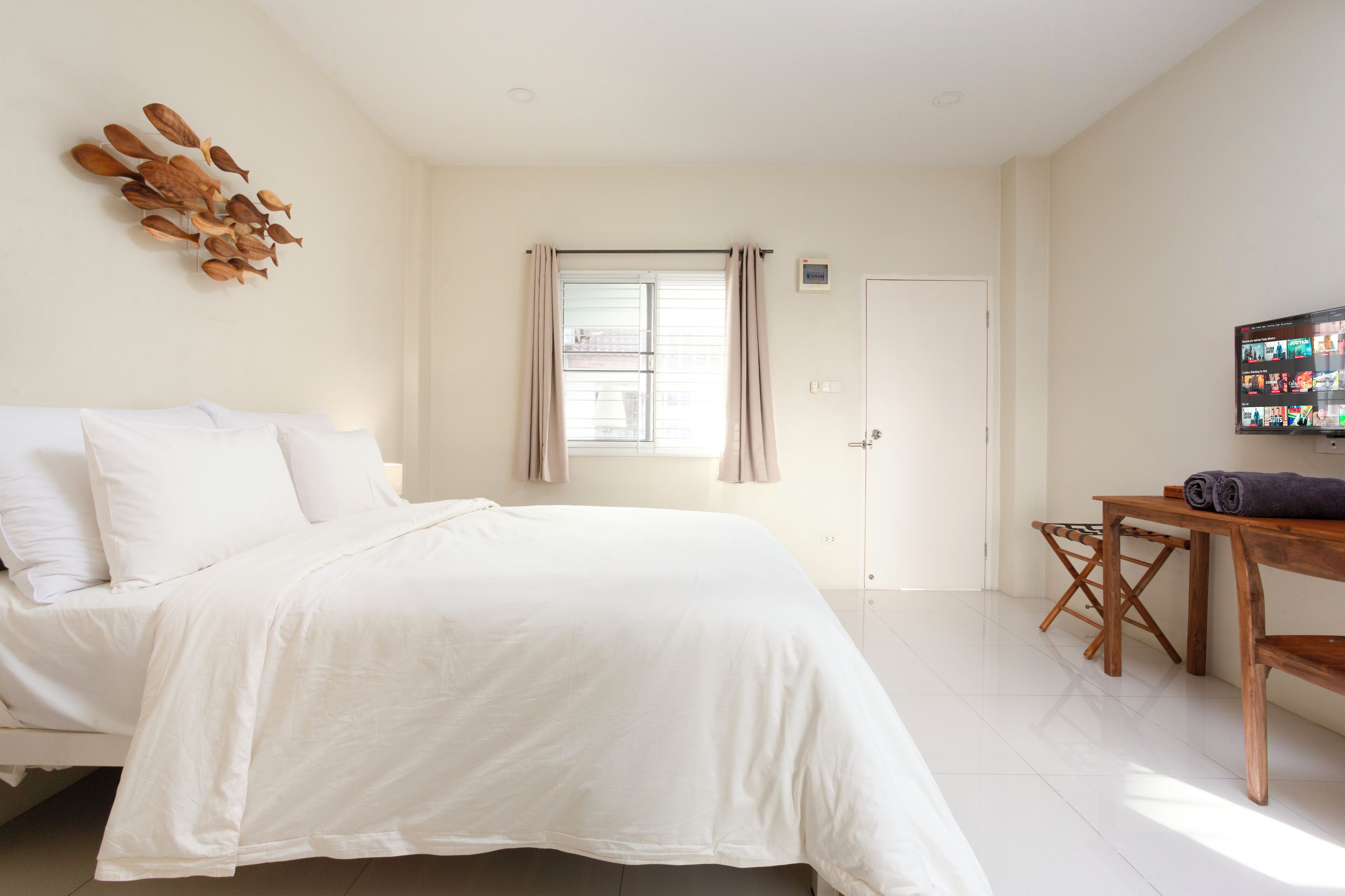 A bedroom with a bed, a wooden table, a TV, and a window with curtains.