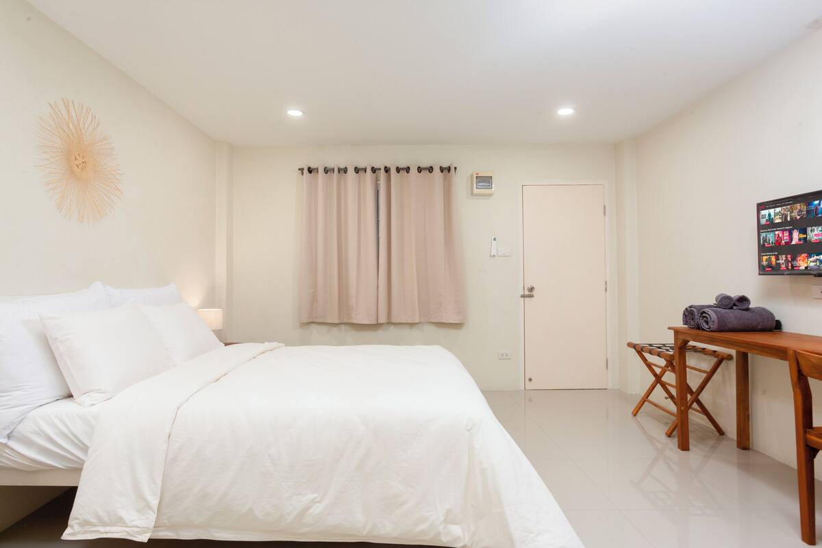 Un dormitorio con cama, una mesa de madera y un televisor instalado en la pared.