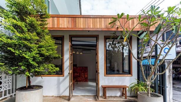 A building entrance with a wooden overhang, potted plants, and a bench. - Comfy Corner Hotel (Chiang Mai)