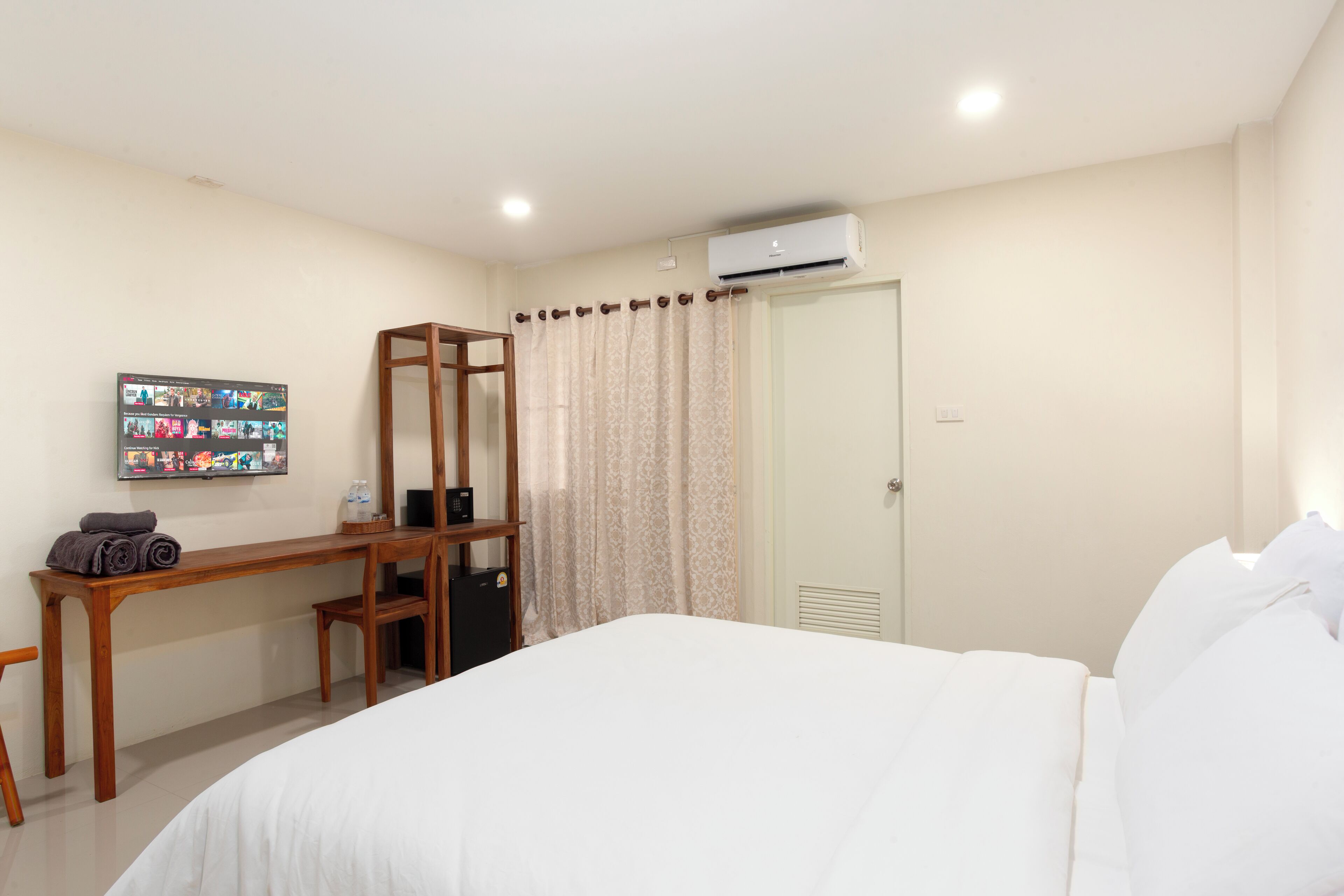 A hotel room with a bed, a desk, a chair, a wardrobe, and an air conditioning unit.