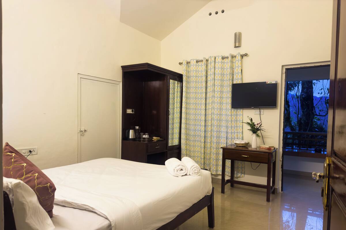 A hotel room with a bed, a wardrobe, a small table with a vase, and a television.