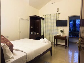 Une chambre d’hôtel avec un lit, une armoire, une petite table avec un vase et un téléviseur.