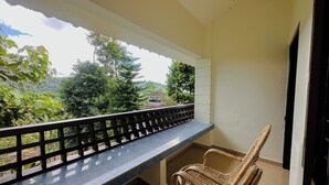 Ein Balkon mit Blick auf Grünflächen und ein Gebäude in der Ferne. Zwei Korbstühle und ein kleiner Tisch sind vorhanden.