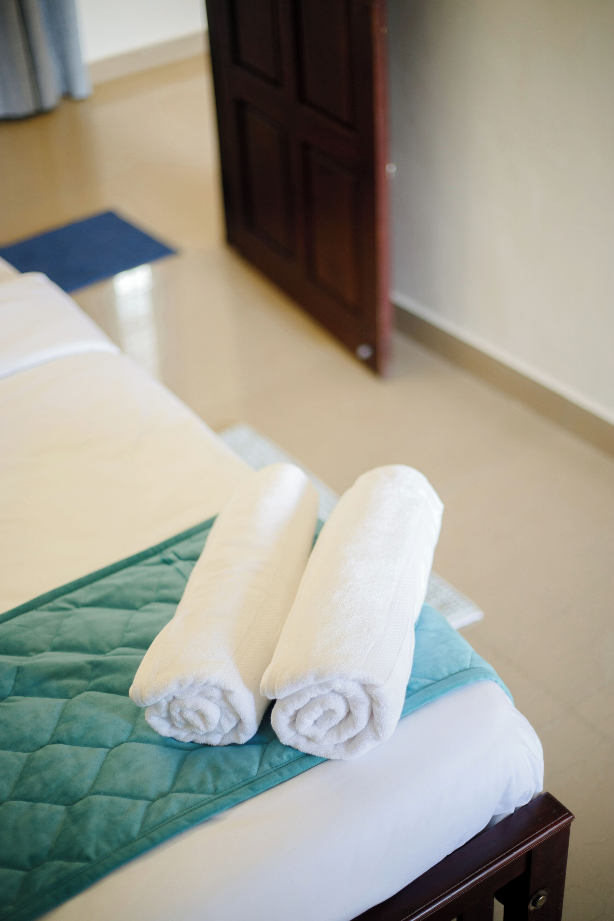 A neatly made bed with a green quilt and two rolled white towels.