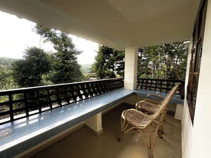 Un balcon doté d’un long comptoir et de deux fauteuils en osier, offrant une vue sur un jardin luxuriant et un bâtiment situé au loin.