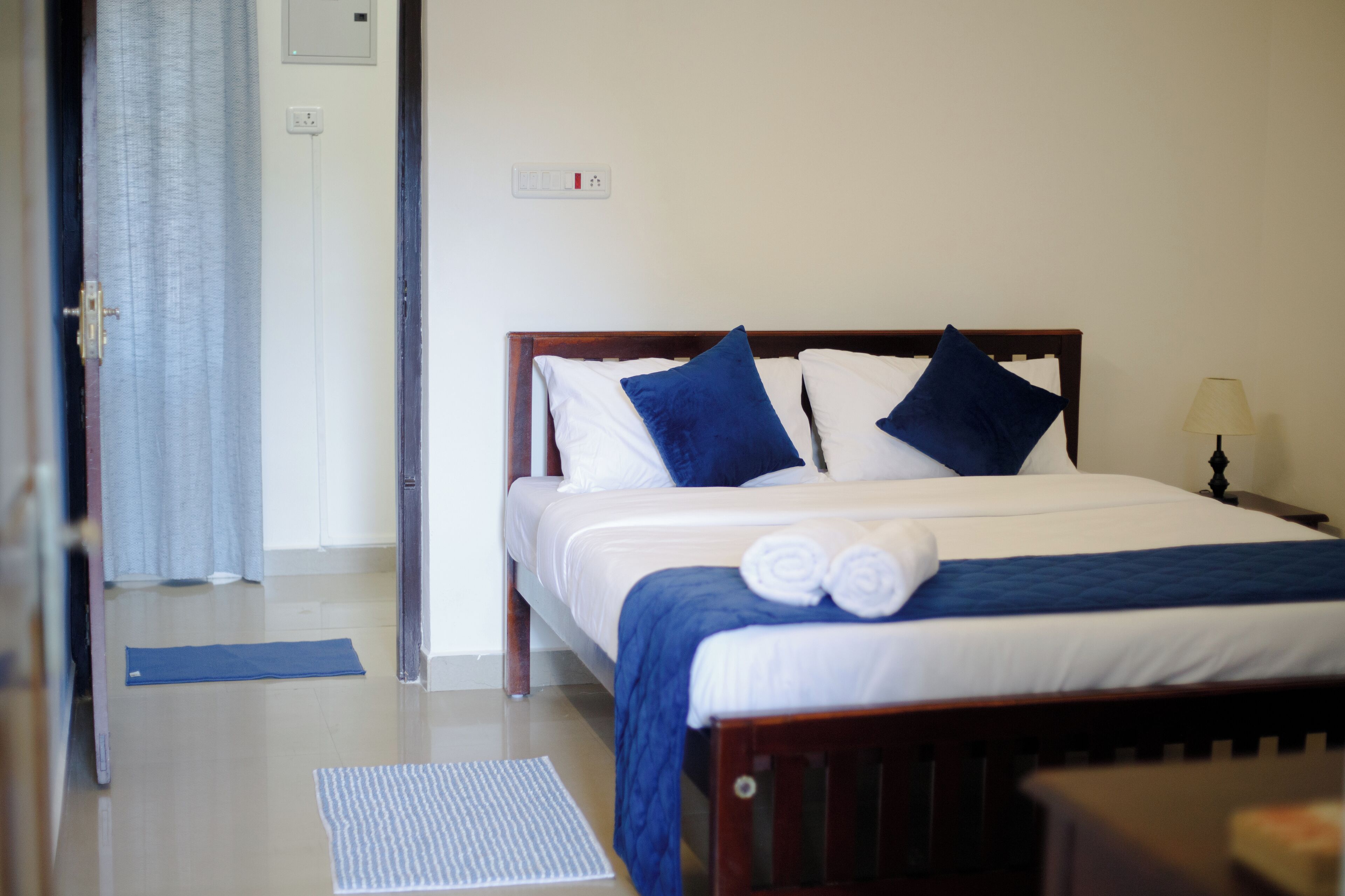A neatly made bed with blue and white bedding, a bedside lamp, and a rolled towel on the bed.