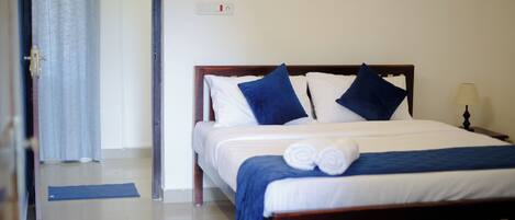 A neatly made bed with blue and white bedding, a bedside lamp, and a rolled towel on the bed.