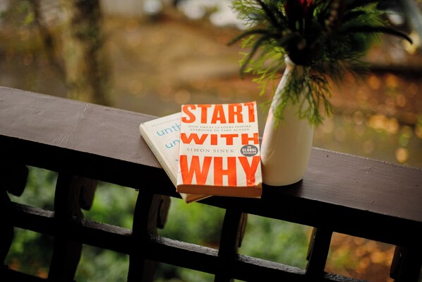 A book titled "START WITH WHY" by Simon Sinek on a wooden railing with a blurred outdoor background.