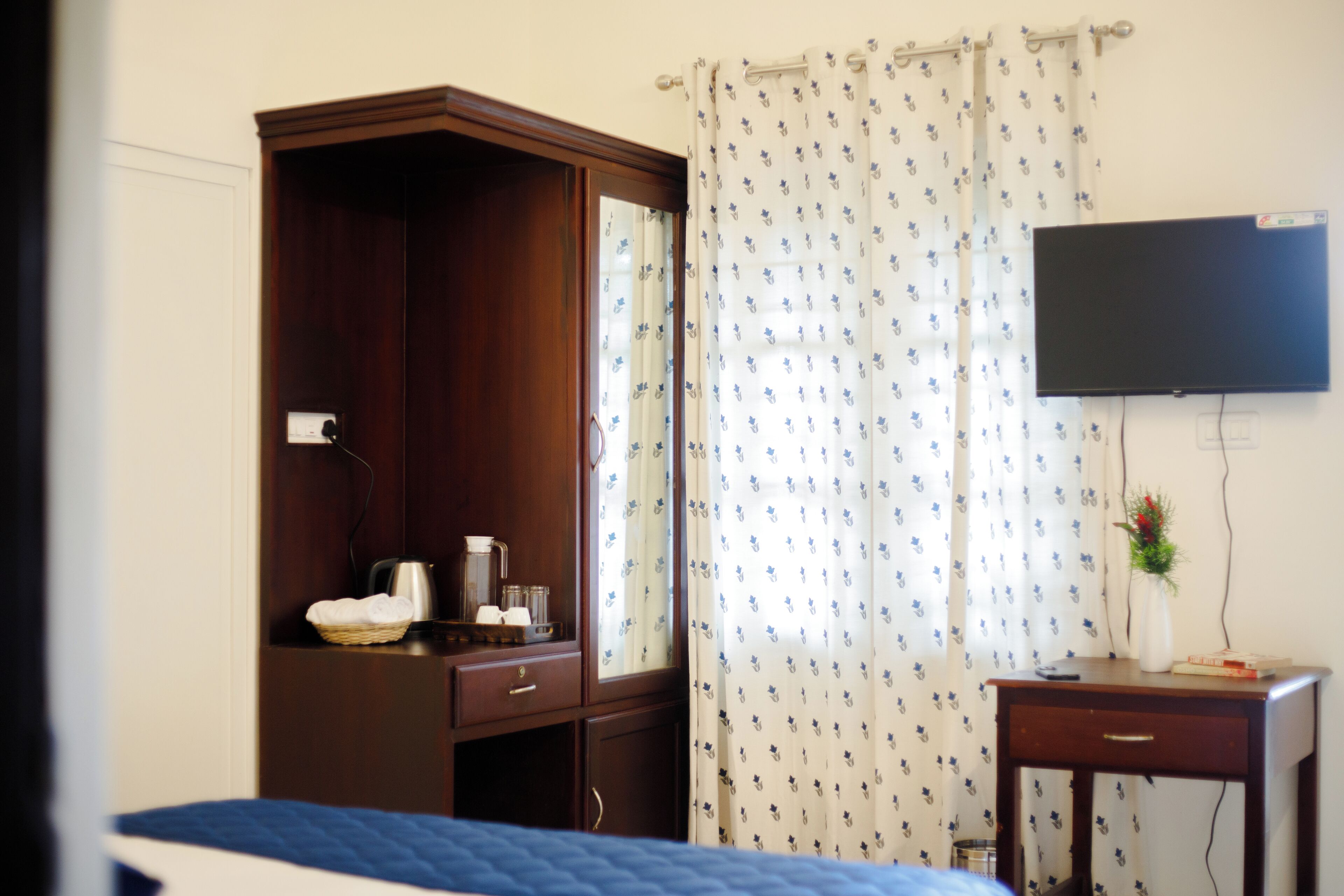 Een hotelkamer met een houten garderobe, een bureau met een flatscreen-televisie en een bed met een blauw deken.