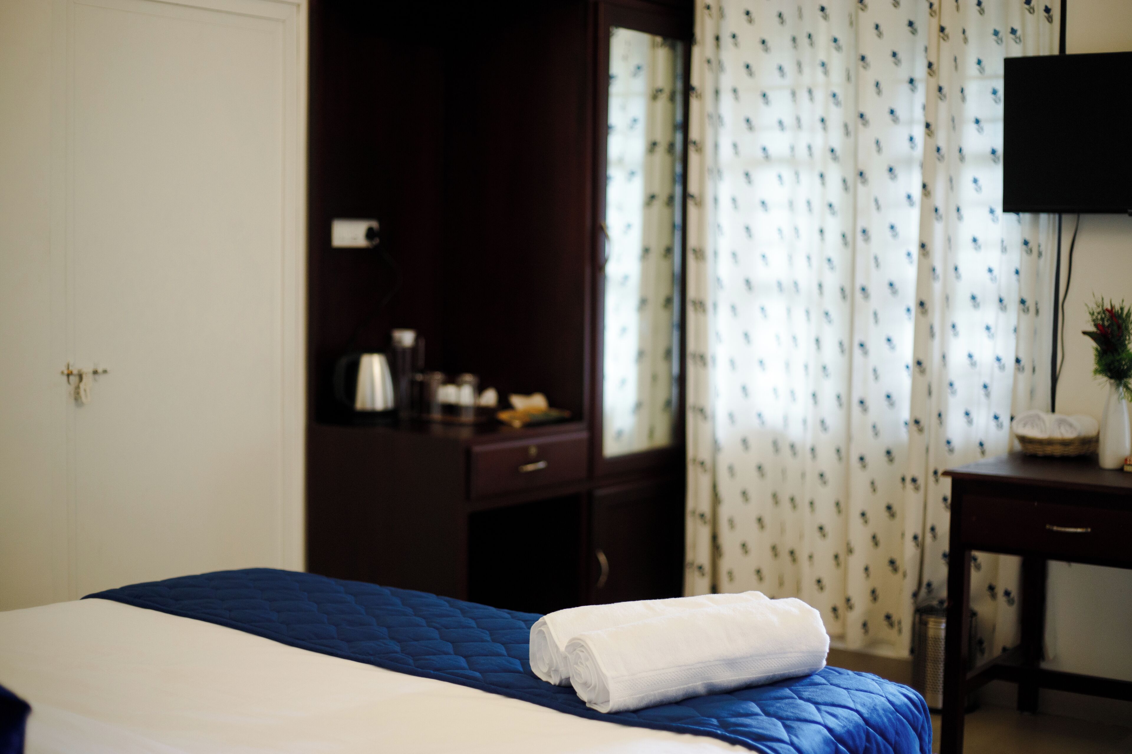 Una habitación de hotel con cama, escritorio, televisor y ventana con cortinas.