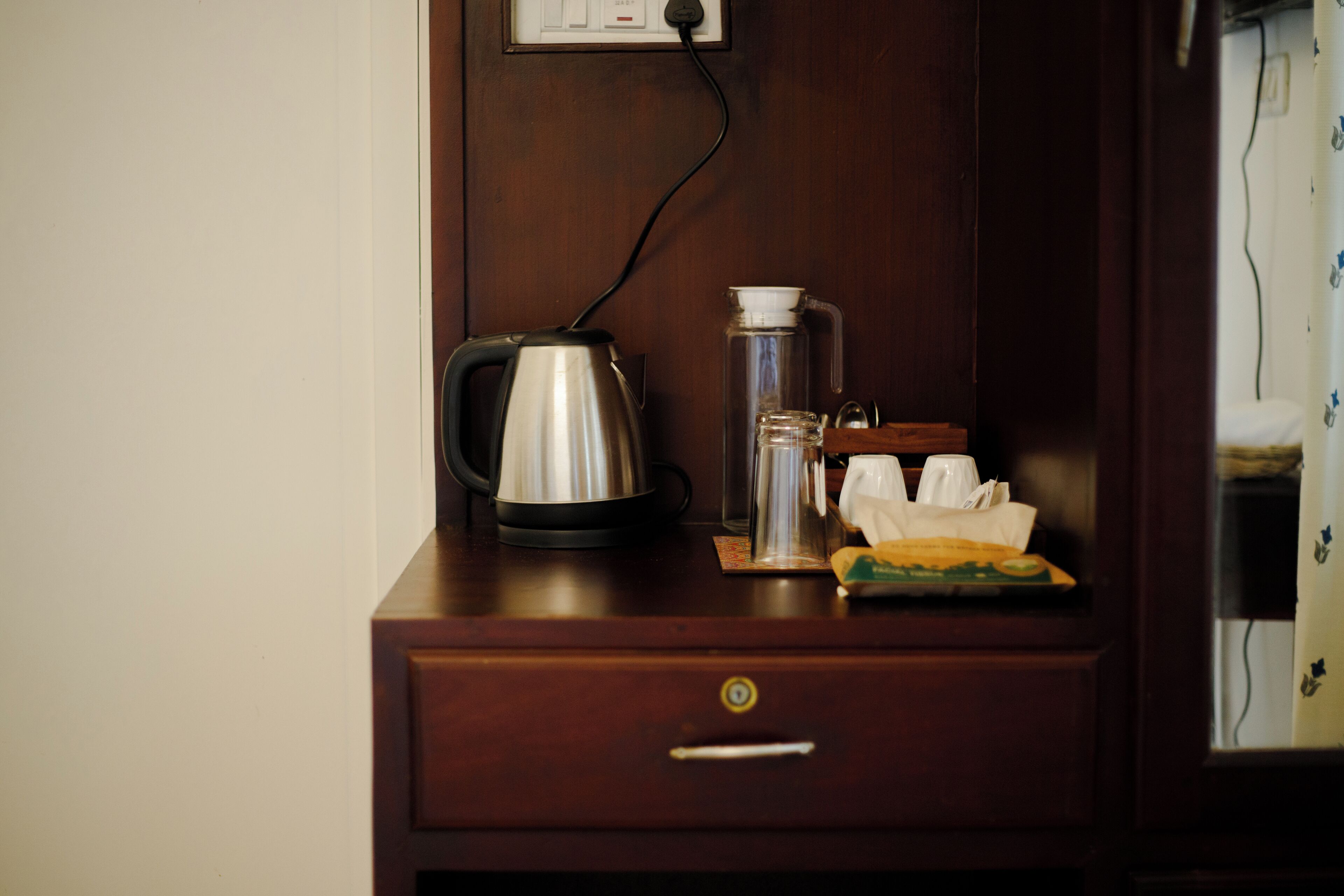 A wooden nightstand with a kettle, a thermos, and a tissue box.