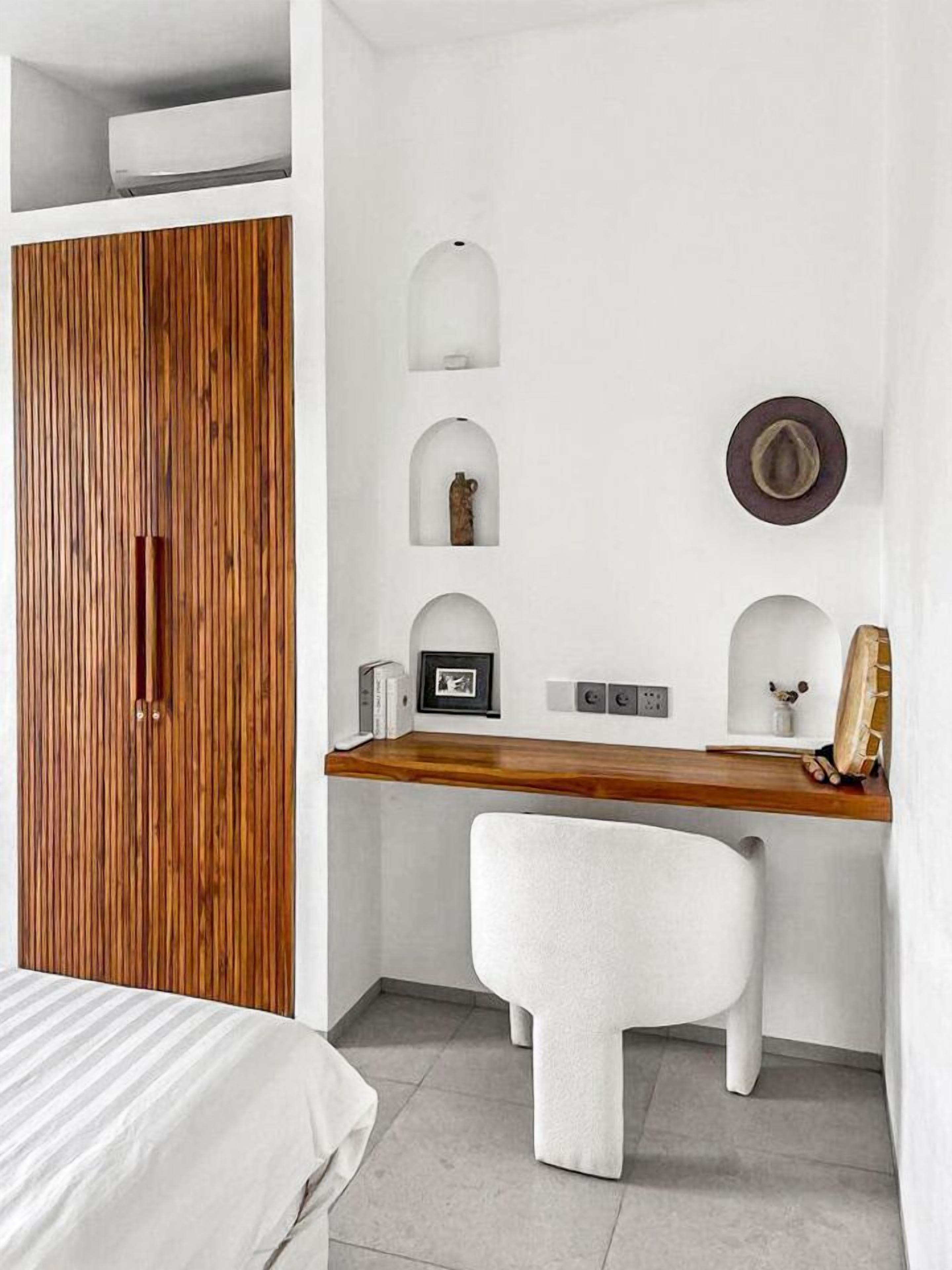 Une chambre avec une armoire en bois, un bureau blanc avec une chaise et un lit recouvert d’une couvre-lit à rayures.