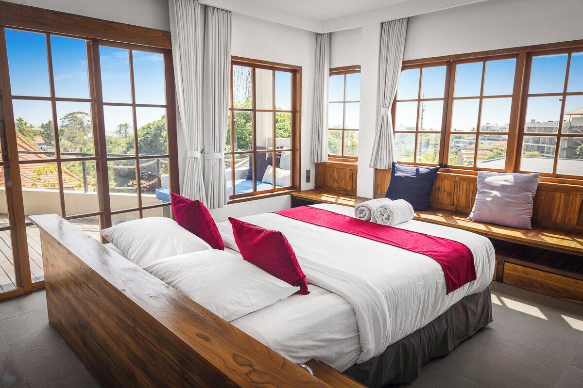 Une chambre d’hôtel avec un grand lit, un banc en bois et une vue sur l’extérieur.