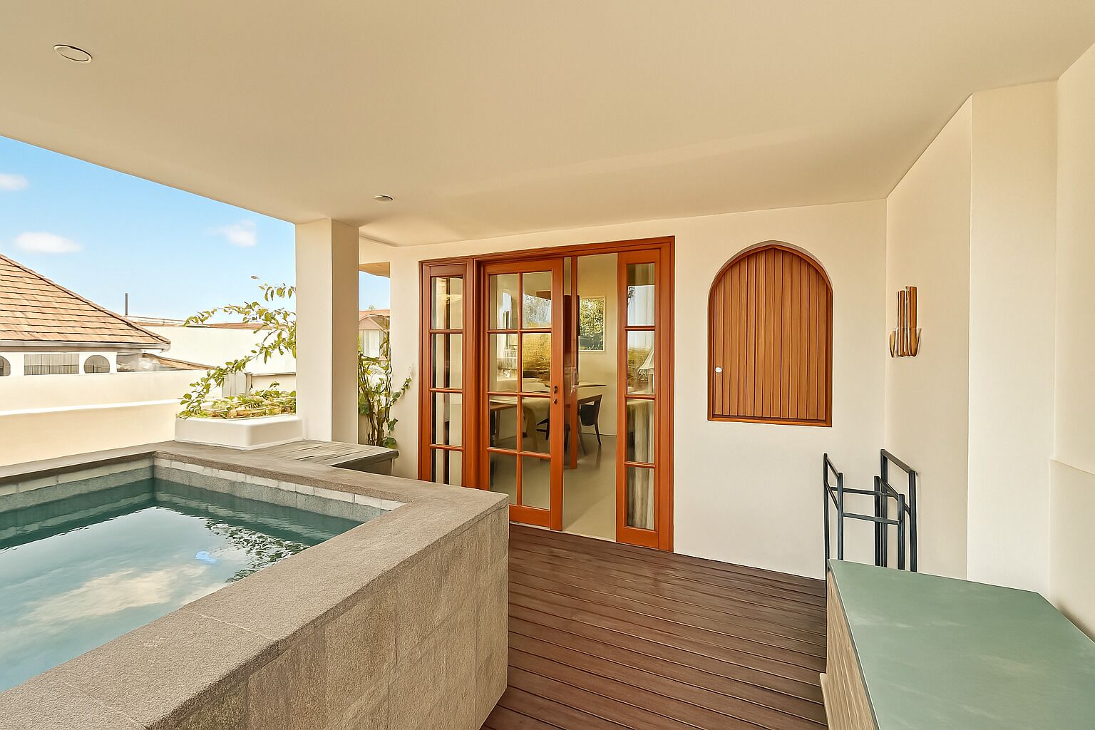 A pool area with a stone edge, wooden deck, and a sliding glass door leading to an indoor space.
