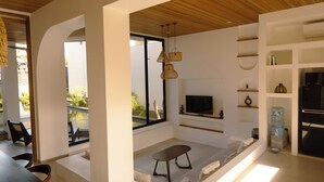 A modern living room with a TV, seating area, and a large window overlooking a pool. - Samastiti Bingin (Pecatu)