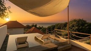 A rooftop infinity pool with two lounge chairs, a wooden deck, and a view of the ocean at sunset. - Samastiti Bingin (Pecatu)