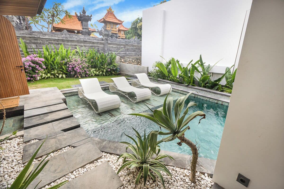 Un espace piscine extérieur moderne, doté de chaises longues, d’un chemin en pierre et de plantes tropicales.