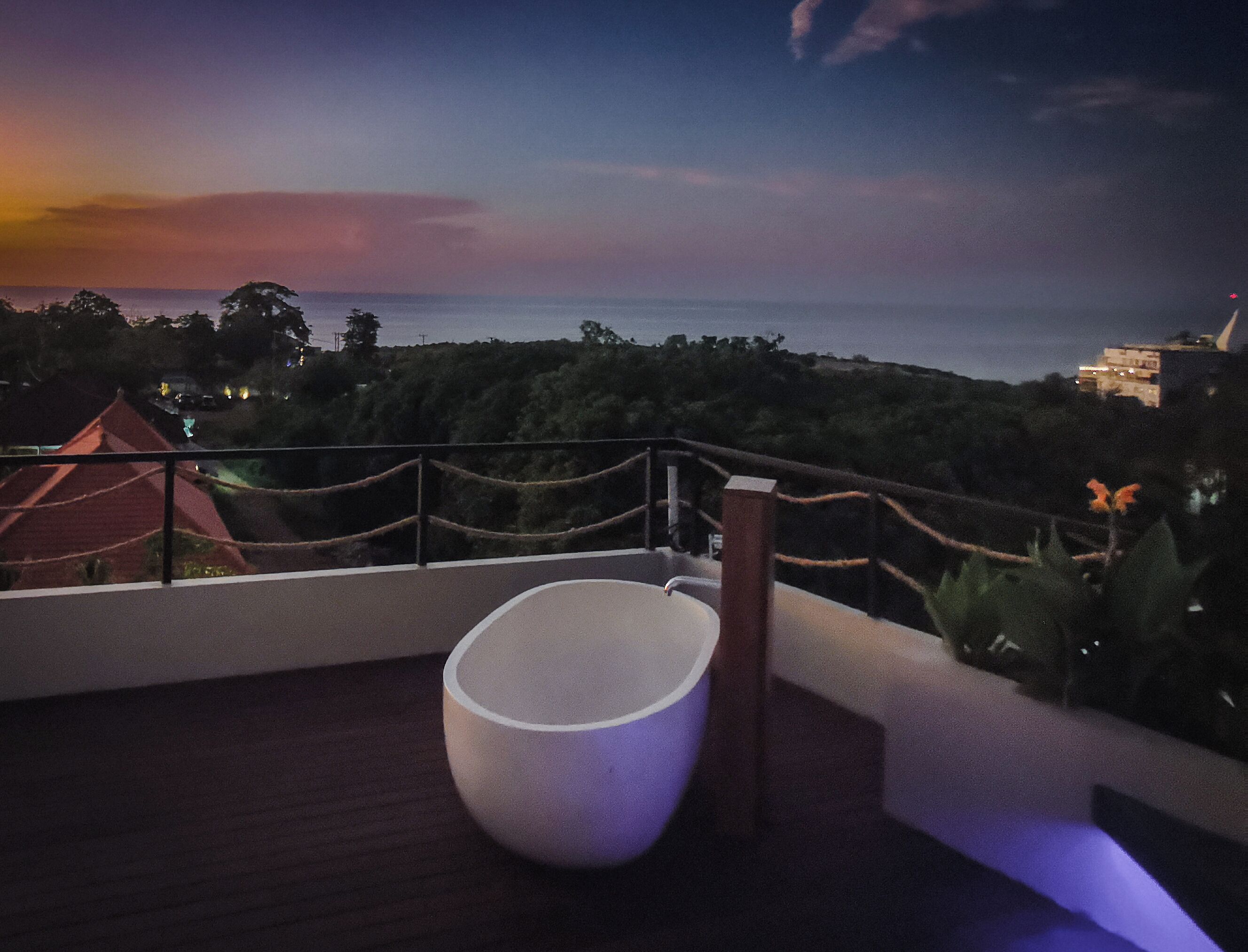 Un balcone con una sedia bianca, una ringhiera e vista sul mare e edifici in lontananza.