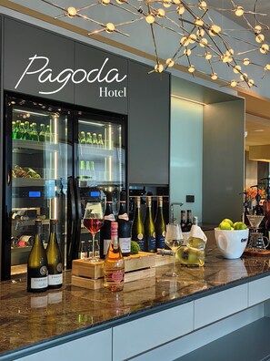 A minibar with wine bottles and glasses, a minibar refrigerator, and a bar area with bottles and a bowl of fruit. - Pagoda Design Hotel Hangzhou Binjiang CBD (Hangzhou)