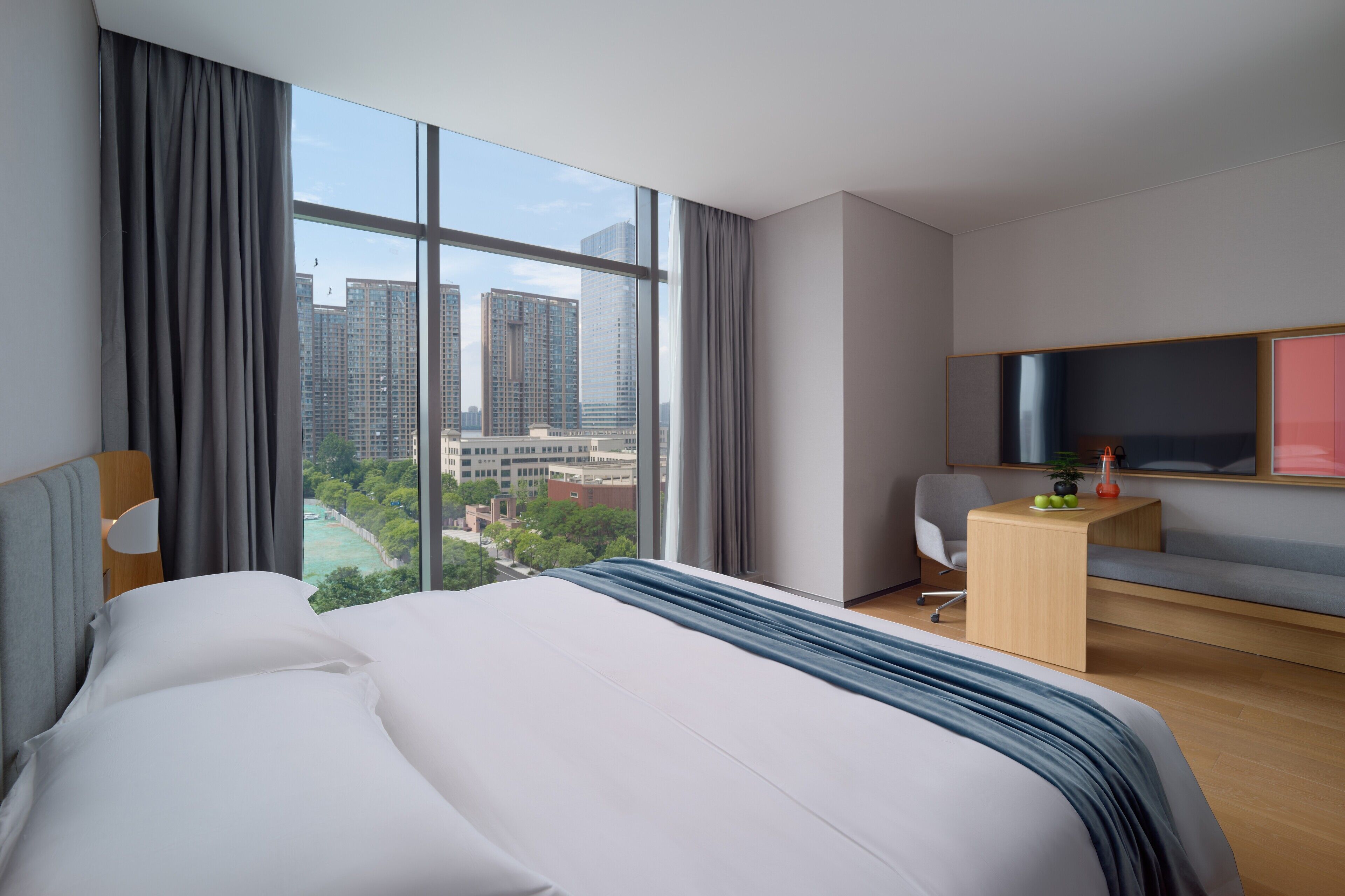 A modern hotel room with a large bed, a desk, a chair, and a TV.