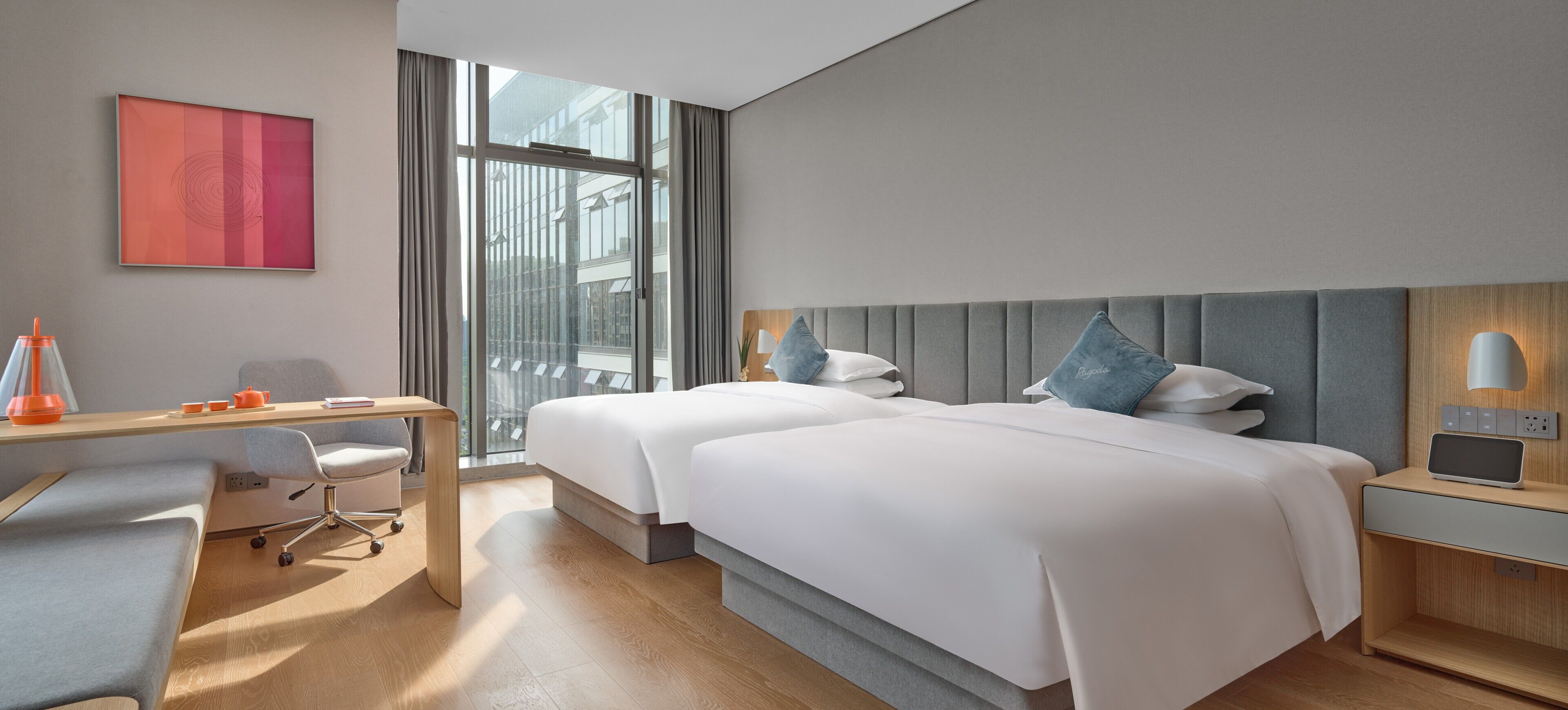 Habitación de hotel con dos camas, un escritorio, una silla, una lámpara y vistas a la ciudad.