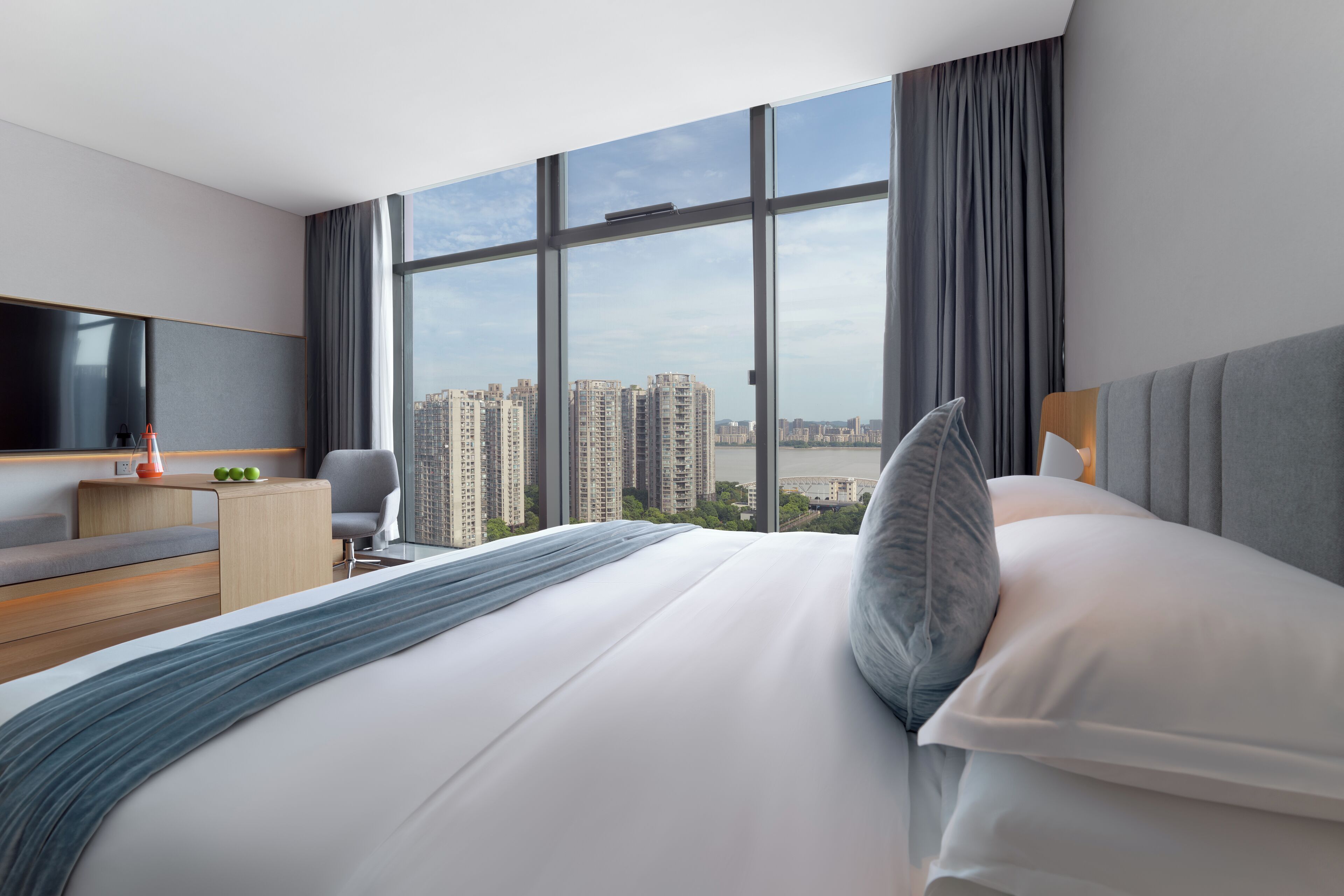 A modern hotel room with a large bed, a desk, a chair, and a TV.